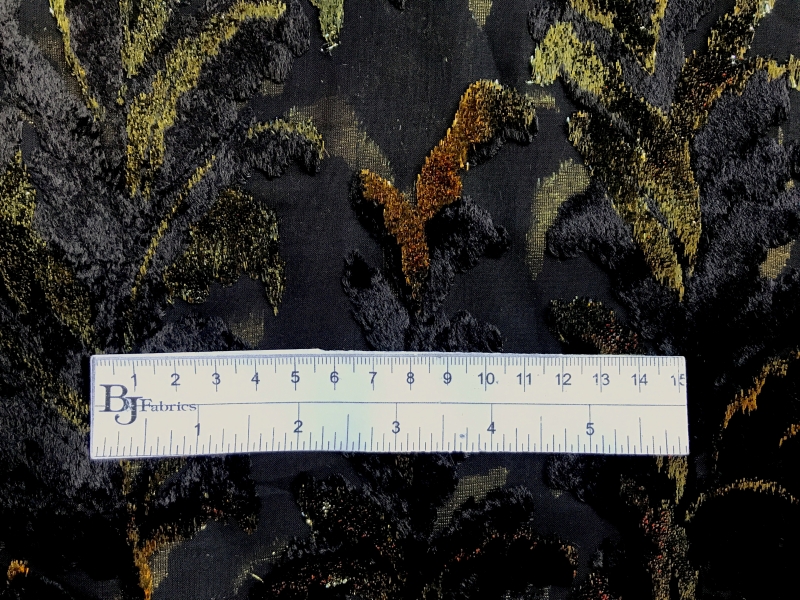 ruler sits on top of black chiffon with burnout velvet in navy and gold lurex in leaves patterns to show scale